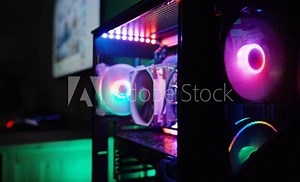 Dark room with a gaming computer with a transparent side panel revealing internal components with RGB lighting and a monitor in the distance.