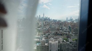 A view of Manhattan through a glass window. A hand gently pulls down the blind, gradually hiding the cityscape. New York vacation. City skyscrapers view with a lot of buildings. beautiful travel day