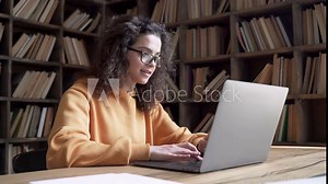 Smiling young hispanic teen girl college student using laptop computer typing on pc working from home office or studying on tech device in classroom sit at desk. Online education, elearning concept.
