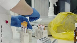 Doctor opens multiple blood test tubes held in the trays. Nurse screws the lids off the blood test tubes. Researcher throws the small caps of the blood test tubes into the yellow bag. Specimen.