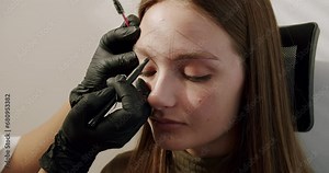 Beauty master doing shape of eyebrows for client woman before henna dyeing. Closeup on female face with prepared brow contour for microblading or permanent makeup at salon