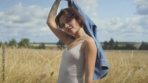 Adorable woman with short hair wearing bodysuit holding jeans jacket on her hands standing on the wheat field. Confident carefree girl outdoors. Real people series.