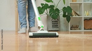 Cleaning room with modern wireless vacuum cleaner without cord. A man in jeans vacuums sawdust from the floor with a modern wireless vacuum cleaner. Man removes sawdust from floor with vacuum cleaner.