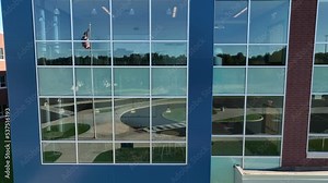 Rising aerial shot of modern classrooms with reflection of American flag in windows. New public high school has modern classrooms and bright natural light from windows.
