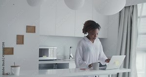 medium shot of a young african lady singing song happily walking towards desk working on computer dancing enjoying music using smartphone then walking away moving body following her humming