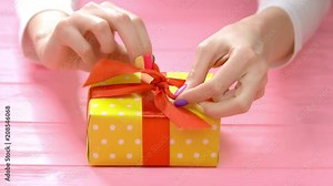 Manicured hands ties ribbon on gift box. Young woman with beautiful manicure packing gift box with red ribbon. Holidays and celebrations concept.