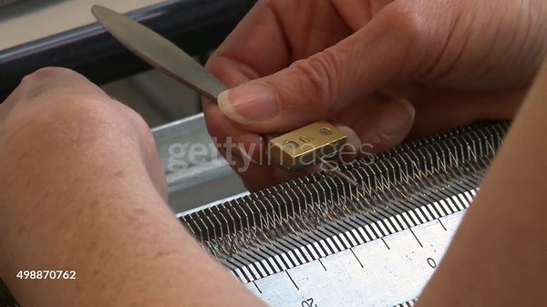 A close shot of a woman using a tool to adjust loops on a knitting...