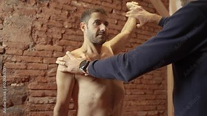 Osteopath assessing shoulder mobility of male patient, manual therapy examination in modern clinic setting