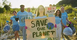 A Caucasian female volunteer protesting againts planet pollution. A group of multiethnic eco acivists walking with the collected garbage and the Save Our Planet poster. Environmental conservation.