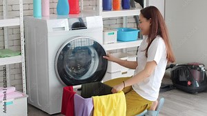 Asian Young Woman in Homely Clothes Sitting in Front of a Washing Machine. She Loads the Washer with Dirty Laundry. Stock Video