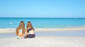 Adorable little girls playing with sand on the beach. Kids sitting in shallow water and making a sandcastle