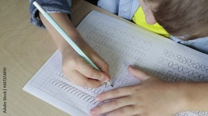Child boy writing different lines with pencil. Prewriting practice to prepare hands for write letters. Children education concept. View from above