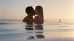 romantic couple kissing in swimming pool enjoying honeymoon vacation...