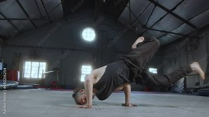Professional male gymnast showing acrobatic performance on camera in a large training gym. He doing acro dance with elements of breakdance