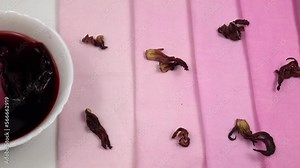 Bowl of rosellelie sepals broth (hibiscus sabdariffa flower) and dried sepals of the hibiscus are on the samples of cotton fabric in gradient purple color, background. Natural dyeing for fabrics,