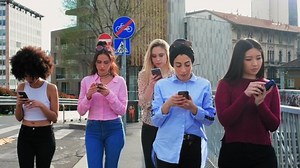 A group of girls, young women walking on a city street, all looking at their phones, phubbing each other.
