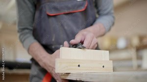 Close-up of unrecognizable professional carpenter attach wooden construction to workbench with clamps and cutting it with small hand saw