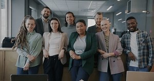 Portrait of cheerful men and women colleagues standing in shared office smiling looking at camera. Workplace and professional occupation concept.