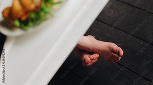 There is breakfast food on the table and the guy's legs are visible under the table. The guy has breakfast in the kitchen in the morning
