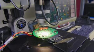 A microchip being inspected under a microscope with a computer