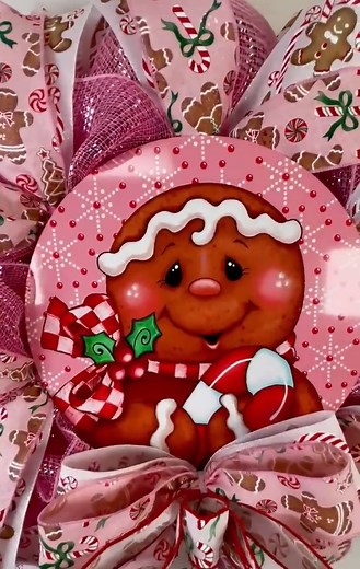 This beautiful Pink Gingerbread Christmas Mesh Wreath is made with pink shimmery deco mesh and an adorable metal gingerbread sign. The sign features a a gingerbread man holding a candy can and he is sitting on a pink and red snowflake background. The wreath has pink, white, red, brown and red colors in it. The ribbons are adorable in pink and white, with candy canes, gingerbread men, and candies. There is a beautiful matching bow. This is a slim wreath that fits small places. Great for a glass s