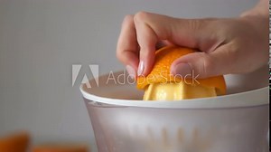 Woman is squeezing oranges using electric juicer in the kitchen, hand closeup. Healthy vegan ripe fruit juice, natural vitamins from food. Making orange juice pressing half of orange.