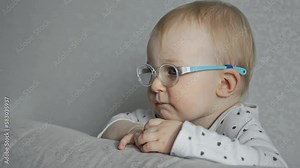 Serious one year old baby with strabismus and glasses is watching TV at home. Caucasian infant has squint or poor eyesight. White kid has an eye disease, bad vision. Portrait of small child