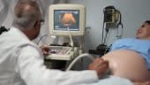 Obstetrician using ultrasound scanner on pregnant young woman in his...
