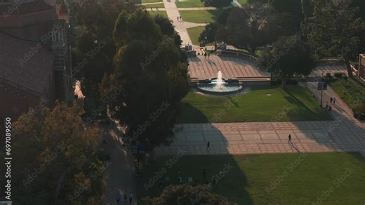Aerial view of UCLA campus bathed in golden light, showcasing Romanesque Revival and Gothic architecture amid lush greenery, with Royce Hall as the centerpiece.