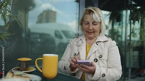 Business freelance 50s blonde woman using smartphone for talking, reading and texting while sitting on table in cafe. Lifestyle smart beautiful women working at coffee shop concepts.