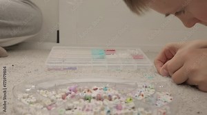 close-up of hands of boy and girl sitting on carpet, threading beads onto string to make bead bracelets and other jewelry. Concept of children's activities at home and developing fine motor skills