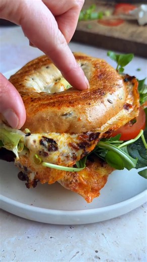 Emily Lloyd | Quick, easy + fuss free recipes on Instagram: "EGG & CHILLI CRISP BAGEL 🥯 Have seen a few people cooking bagels with eggs like this and I had to try my own version! I first added chilli crisp to the pan, then 2 beaten eggs, follow with the bagels face down and spring onions. Once the egg is cooked through, flip over, top one half with tomato and feta, and the other with green leaves. Fold together and dig in. So good as a quick, easy vegetarian breakfast, brunch or lunch. DIVINE."