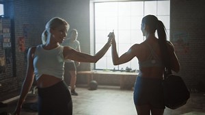 Following Shot of the Beautiful Athletic WomanWalking into Hardcore Gym, Greets Her Friends and Fellow Athletes. Ready for Her Power Workout, Strength Exercise and Bodybuilding Training Session