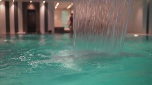 Waterfall in the pool. Girl on the background of the pool.