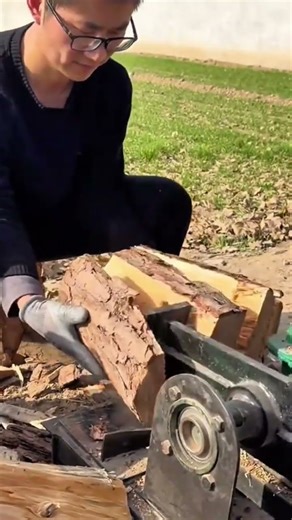 Man holding a log against a motorized screw splitter to break firewood