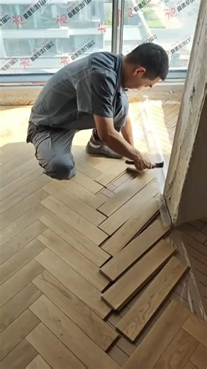 worker uses a hammer to install light wood planks in a herringbone pattern