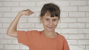 The child shows strength. Athletic little girl shows muscles.