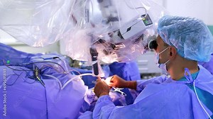Neurosurgeon stands looking into neuro microscope using the metal tools. Top view on the professional performing operation.