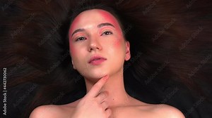 Beautiful young model posing for a photographer. Fashionable model with bright makeup on a black fabric background. 4k footage