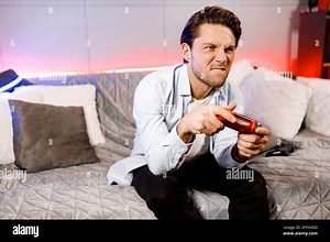 Concentrated guy playing video game, holding remote red controller, enjoying leisure time with device, engaged in online competition with friends Stock Photo - Alamy