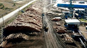 dolly forward zoom drone shot over loaded logging semi truck driving forward between log piles while log loader is backing up at a sawmill in a desert environment