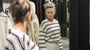Woman trying on clothes in fitting room after shopping spree. Discover her shopping haul and see her trying on various outfits in real time. Experience excitement of post shopping wardrobe selection.