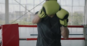 Slow motion portrait of muscular sportsman boxer training in gym punching air with gloves and looking at camera. Martial arts and sports concept.