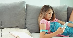 School girl using cell phone, laughing, lying on the sofa