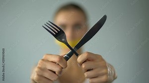 Woman closed mouth with tape-line, crossing fork and knife, stop diet, anorexia