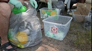 Medium full shot of legs of unrecognizable multiethnic eco activists sitting on stools in forest or park, sorting plastic rubbish into labeled containers for recycling at community litter pick event