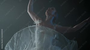 graceful ballerina doing a workout in the classroom. Smoke, fog, ballet dancer in white tutu, girl in pointe, whirls around in the dark with light on the black background.