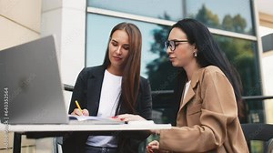 Successful business women partners work remotely on the cafe terrace. Businesswomen at a business meeting in an outdoor restaurant discussing a project on a laptop
