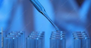 Closeup of scientist using pipette to add blue liquid to test tube in laboratory