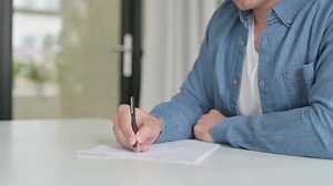 Man Writes on Paper on a White Table